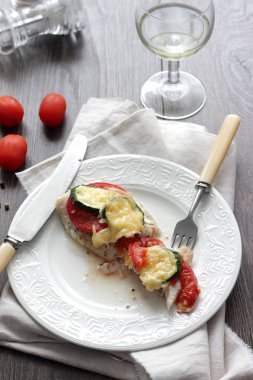 Fırında pişmiş domates, kabak ve peynir bir plaka üzerinde morina balığı fileto