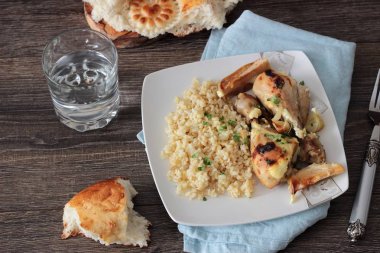 Rustik ahşap zemin üzerinde bir plaka üzerinde elma ve bulgar ile kavrulmuş tavuk budu