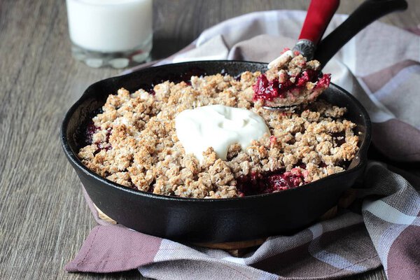 Berry crumble with oatmeal crispy crust with cream in cast iron pan on a wood background.  Healthy breakfast.