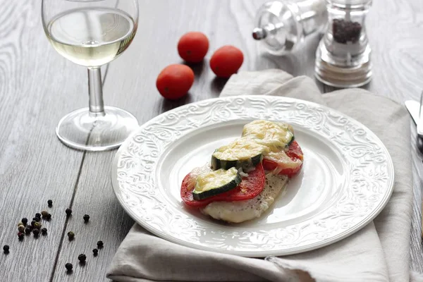 Fırında pişmiş domates, kabak ve peynir bir plaka üzerinde morina balığı fileto