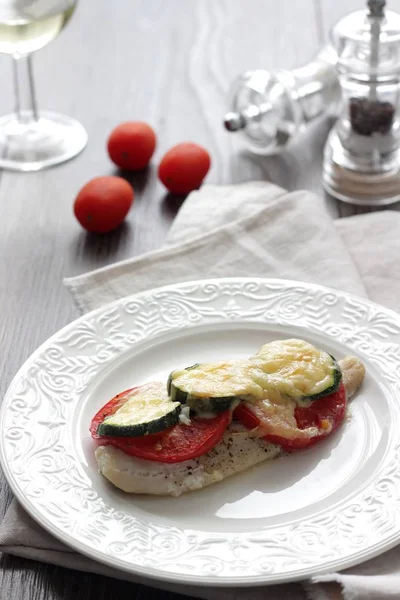 Fırında pişmiş domates, kabak ve peynir bir plaka üzerinde morina balığı fileto