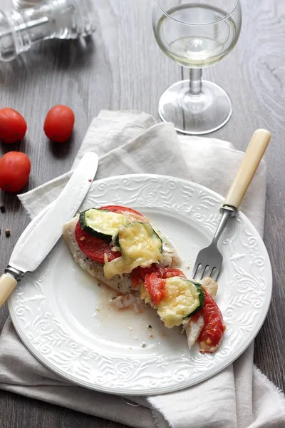 Fırında pişmiş domates, kabak ve peynir bir plaka üzerinde morina balığı fileto