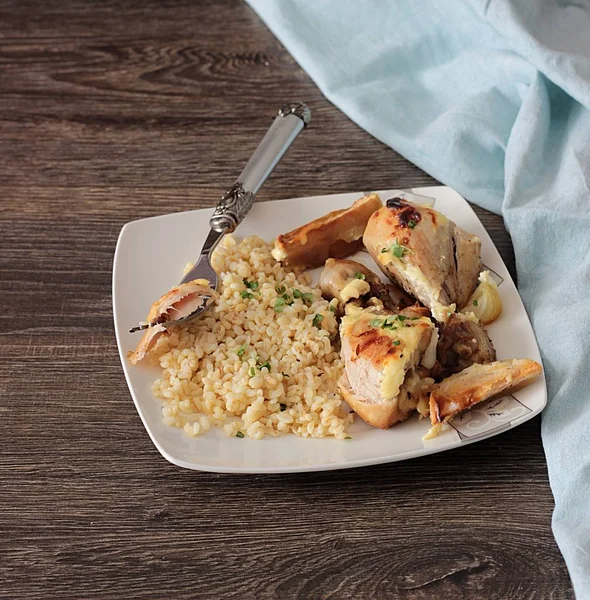 Rustik ahşap zemin üzerinde bir plaka üzerinde elma ve bulgar ile kavrulmuş tavuk budu