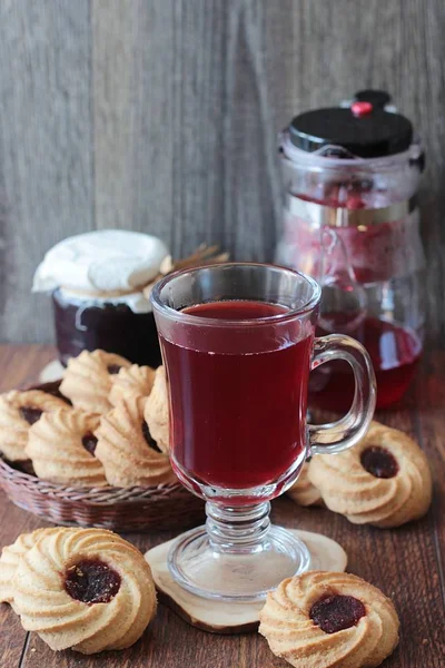 Стіл для сніданку, червоний чай в чайнику і в склянці і печиво з джемом на дерев'яному столі — стокове фото