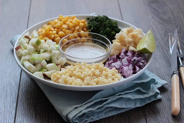 Deliciosa ensalada de pasta de verano en mesa rústica con maíz, manzana, cebolla roja, queso y eneldo — Foto de Stock