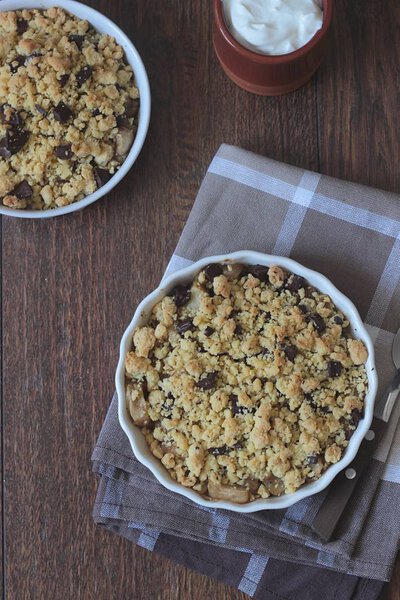 Homemade sweet apple chocolate crumble dessert with cream on the wooden background