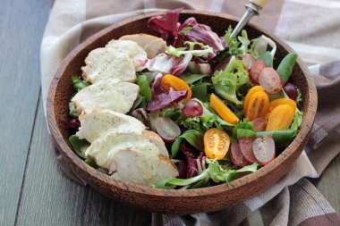 Izgara tavuk fileto, pembe üzüm ve renkli salata karışımı marul yaprakları, hindiba, Mısır salata ve bir masada ahşap bir kasede radicchio ile domates.