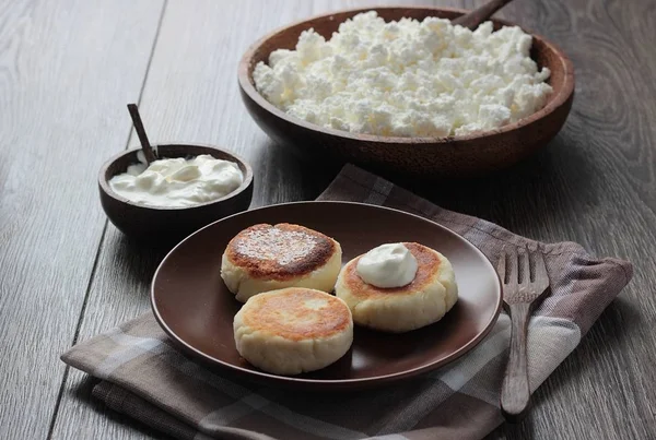 Cottage cheese pancakes (homemade traditional Russian syrniki) with sour cream on brown plate