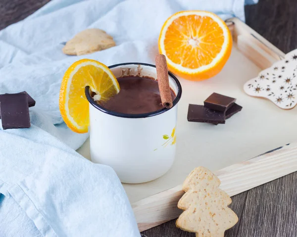 Hot chocolate or cocoa drink with orange and cinnamon stick served with gingerbread cookies and pieces of chocolate.
