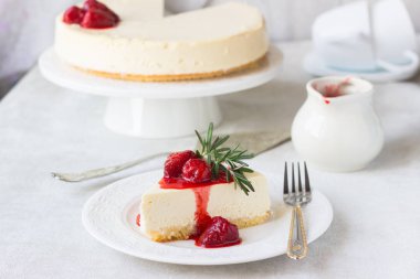 Klasik vanilyalı cheesecake (New York cheesecake) beyaz tabakta çilek sosu ve biberiye ve açık arkaplanlı