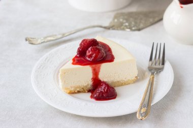 Klasik vanilyalı cheesecake (New York cheesecake) beyaz tabakta çilek sosu ve biberiye ve açık arkaplanlı