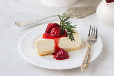 Klasik vanilyalı cheesecake (New York cheesecake) beyaz tabakta çilek sosu ve biberiye ve açık arkaplanlı