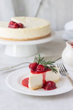 Klasik vanilyalı cheesecake (New York cheesecake) beyaz tabakta çilek sosu ve biberiye ve açık arkaplanlı