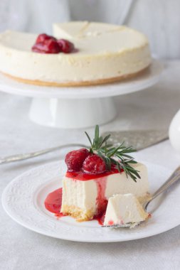 Klasik vanilyalı cheesecake (New York cheesecake) beyaz tabakta çilek sosu ve biberiye ve açık arkaplanlı