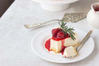 Klasik vanilyalı cheesecake (New York cheesecake) beyaz tabakta çilek sosu ve biberiye ve açık arkaplanlı