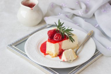 Klasik vanilyalı cheesecake (New York cheesecake) beyaz tabakta çilek sosu ve biberiye ve açık arkaplanlı