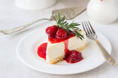 Klasik vanilyalı cheesecake (New York cheesecake) beyaz tabakta çilek sosu ve biberiye ve açık arkaplanlı