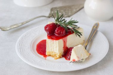Klasik vanilyalı cheesecake (New York cheesecake) beyaz tabakta çilek sosu ve biberiye ve açık arkaplanlı