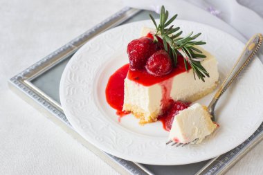 Klasik vanilyalı cheesecake (New York cheesecake) beyaz tabakta çilek sosu ve biberiye ve açık arkaplanlı