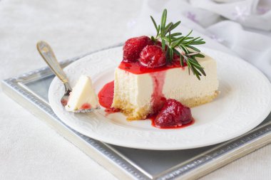 Klasik vanilyalı cheesecake (New York cheesecake) beyaz tabakta çilek sosu ve biberiye ve açık arkaplanlı