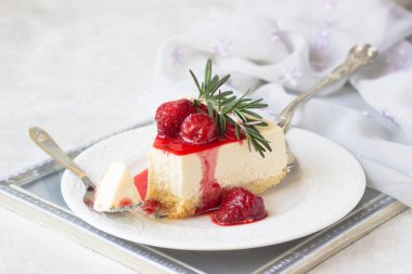 Klasik vanilyalı cheesecake (New York cheesecake) beyaz tabakta çilek sosu ve biberiye ve açık arkaplanlı
