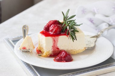 Klasik vanilyalı cheesecake (New York cheesecake) beyaz tabakta çilek sosu ve biberiye ve açık arkaplanlı