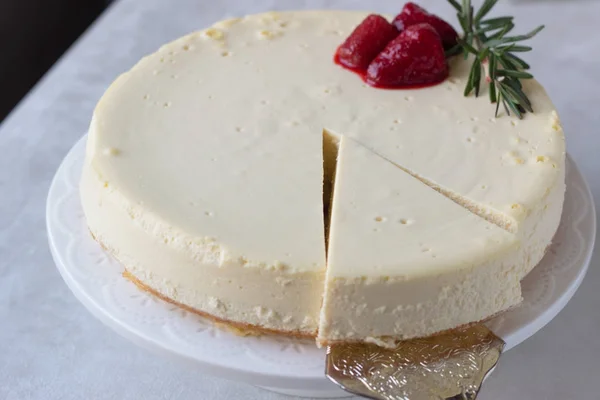 Klasik vanilyalı cheesecake (New York cheesecake) beyaz tabakta çilek sosu ve biberiye ve açık arkaplanlı