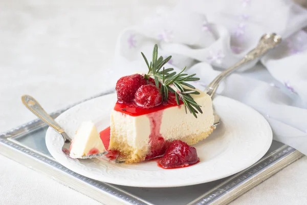Klasik vanilyalı cheesecake (New York cheesecake) beyaz tabakta çilek sosu ve biberiye ve açık arkaplanlı