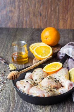 Çiğ gıda. Tavuk budu (sopaları) ahşap masa arka plan üzerinde dökme demir tavada portakal ve hardal Marine ile. İçeriği yemek