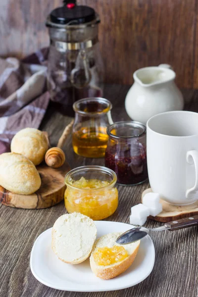 Buns, jam, honey, coffee or tea with milk. Breakfast concept. Delicious breakfast on rustic wooden table.