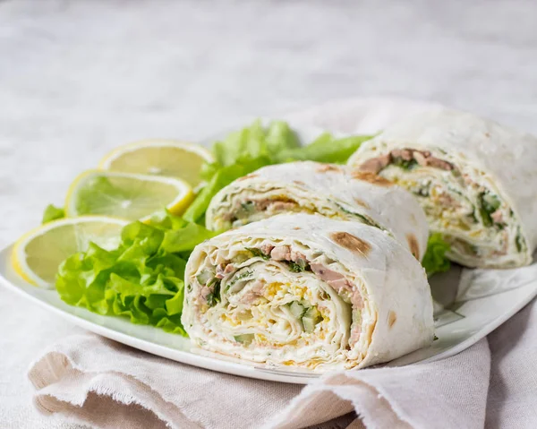Tuna salad roll sandwich with salad leaves on white plate. Roll sandwich with tuna, cucumber, eggs and dill. Thin Armenian pita bread or lavash. Snack.