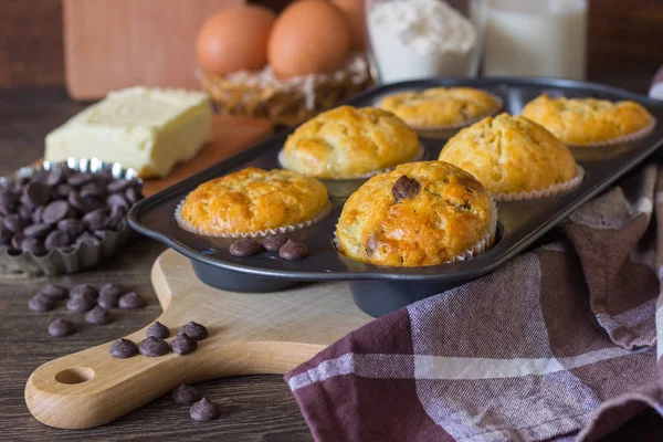 Muffins with chocolate chips (drops) in bakeware (muffin pan) on linen towel. Basic muffin recipe. Homemade muffins for breakfast or dessert.