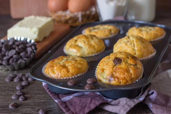 Muffins with chocolate chips (drops) in bakeware (muffin pan) on linen towel. Basic muffin recipe. Homemade muffins for breakfast or dessert.