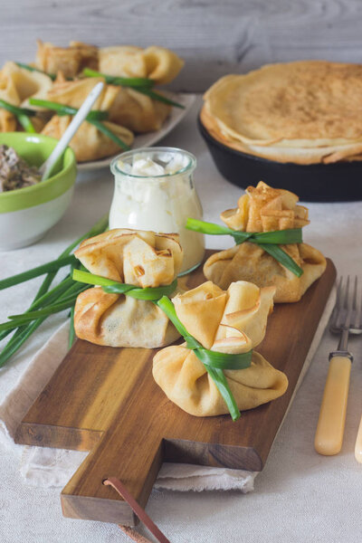 Crepes (pancakes) stuffed with chicken and mushrooms on a wooden cutting board served with sour cream. Traditional food on a pancake week. Traditional dish of Slavic cuisine.