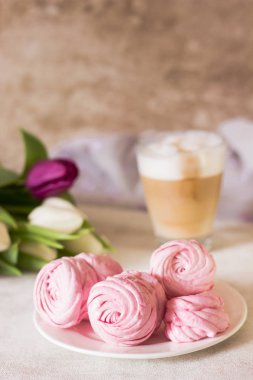 Pembe ev yapımı zephyr veya marshmallow ile fincan cappuccino kahve ve açık gri renkli çiçekler. Hatmi, beze, Zephyr