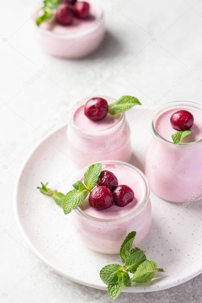 Delicious Italian dessert cherry panna cotta with fresh cherries and mint in jars. Light grey stone background, selective focus. Copy space.