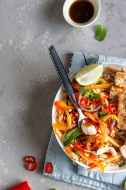 Izgara tavuk ve havuçlu Buda kasesi, kırmızı dolma biber, soğan, pirinç ve açık gri taşlı arka planda otlar. Sağlıklı dengeli beslenme. Rahatlatıcı yemek..