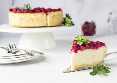 Kızılcık soslu klasik New York peynirli keki, nane ve biberiye, açık gri taş arka plan. 