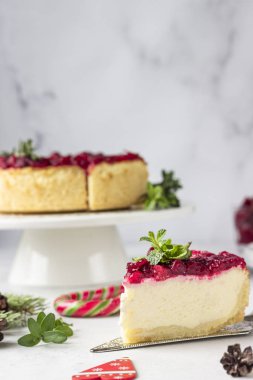 Klasik New York peynirli keki, kızılcık soslu, nane ve biberiye, açık gri taşlı arka plan. Şenlikli Noel süslemesi.