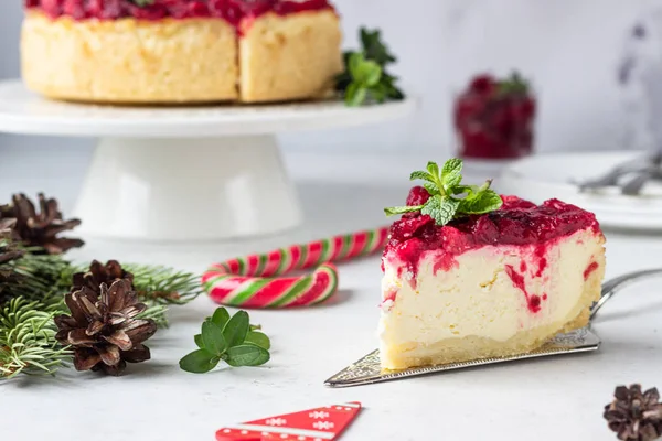Klasik New York peynirli keki, kızılcık soslu, nane ve biberiye, açık gri taşlı arka plan. Şenlikli Noel süslemesi.