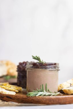 Bir kavanozda taze tavuk ciğeri ezmesi ve soğan turşusu (marmelat), ahşap bir tabakta ekmek ve kraker. Açık gri arkaplan, seçici odak.