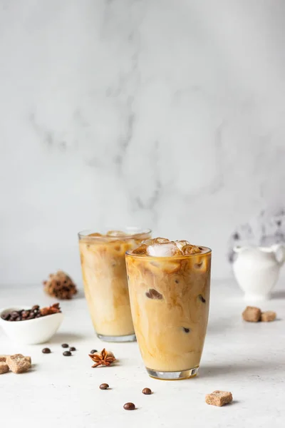 Cold brew coffee with spices and milk on light grey background. Spicy coffee with ice cubes.