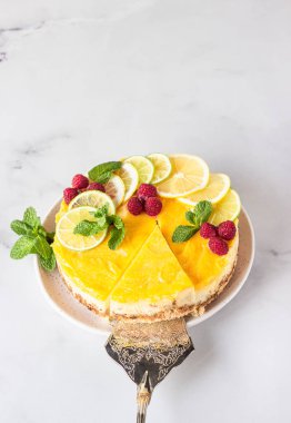 Limon dilimleri, limon dilimleri, donmuş ahududu ve seramik tabakta naneli limonlu vanilyalı cheesecake. Açık gri arkaplan.