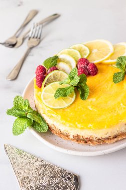 Limon dilimleri, limon dilimleri, donmuş ahududu ve seramik tabakta naneli limonlu vanilyalı cheesecake. Açık gri arkaplan.