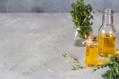 Bir şişe kekik (timüs) taze kekik ve açık gri taş zemin içeren temel yağ.