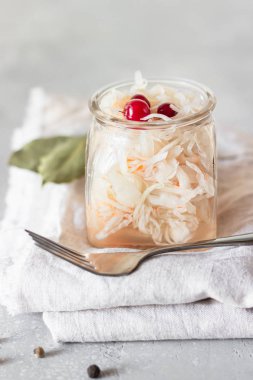 Ev yapımı lahana turşusu. Mayalanmış yiyecek. Cam kavanozda yaban mersinli lahana turşusu ve açık gri beton arka planda çatal.. 
