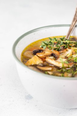 Ev yapımı vejetaryen mantar çorbası. Arpa ve sebzeli. Açık gri taşlı arka planda seramik kasede otlar var. Lezzetli bir ilk yemek, konforlu yemek..