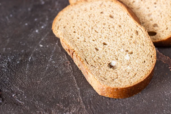 Piece of rye bread with fungus (mold) on a dark brown slate background.