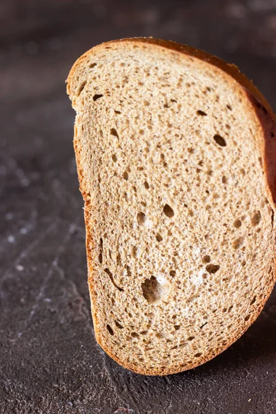 Piece of rye bread with fungus (mold) on a dark brown slate background.