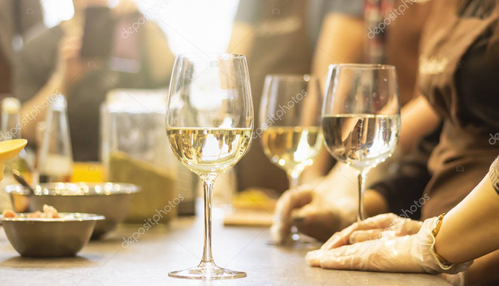 Refreshing white wine in glasses standing side by side on a table with candle in the sun light, blurred background.